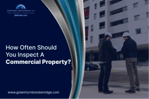 Two inspectors in hard hats reviewing documents outside a large commercial building for a property inspection.